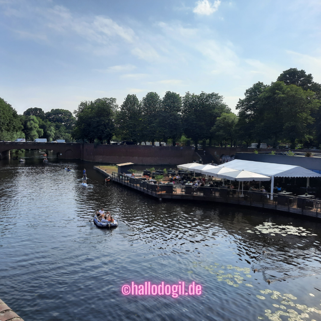 Bild vom Hamburg Stadtpark. Es zeigt den Goldbekkanal mit Booten und das Café Stadtparkterassen.