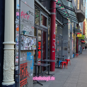 Mauser mit Graffitis und Stickers in der Sternschanze. Daneben eine mit Stuck verzierte weiße Säule
